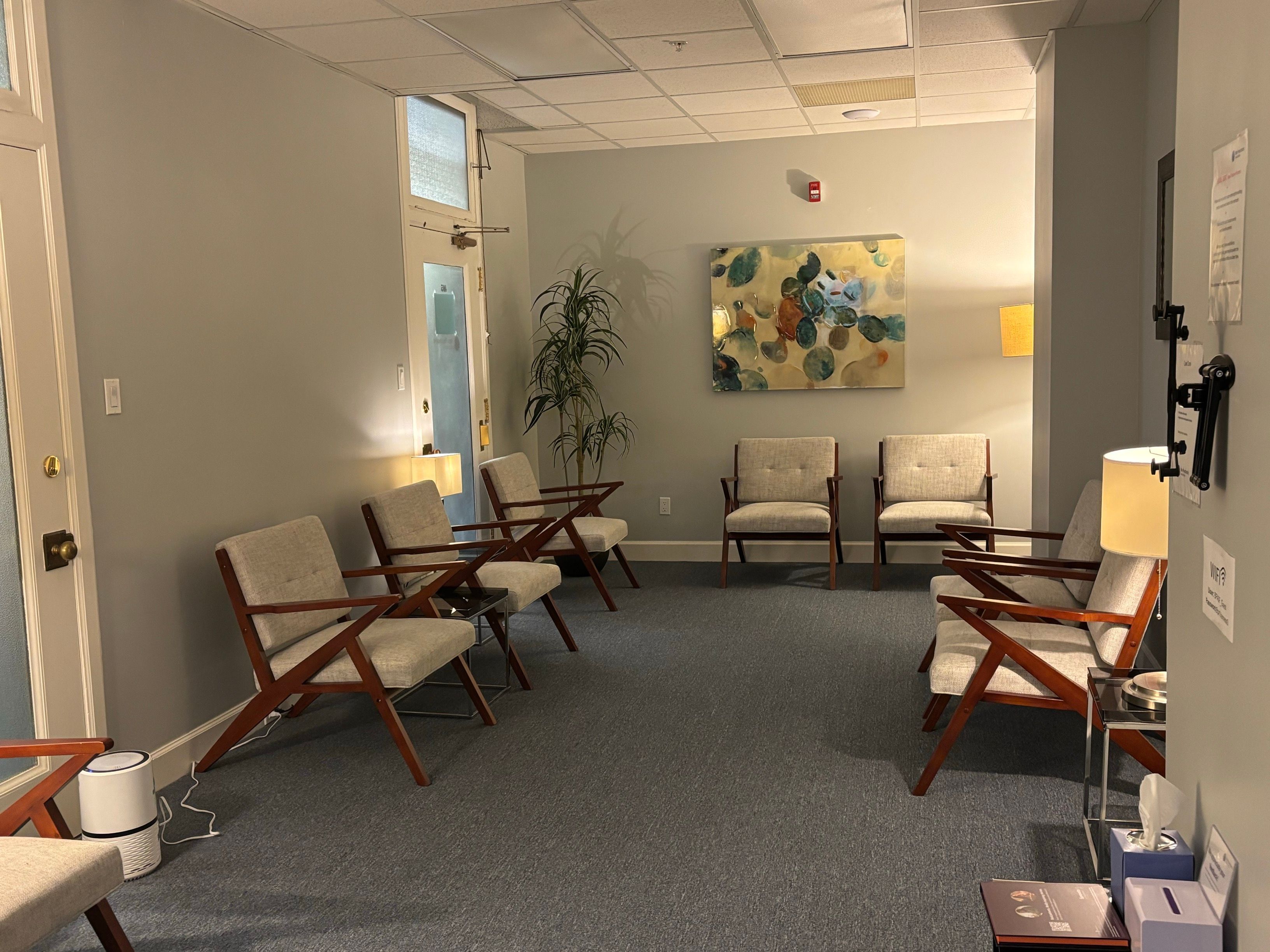 San Francisco waiting room with wooden armchairs, an abstract painting, and a tall plant.