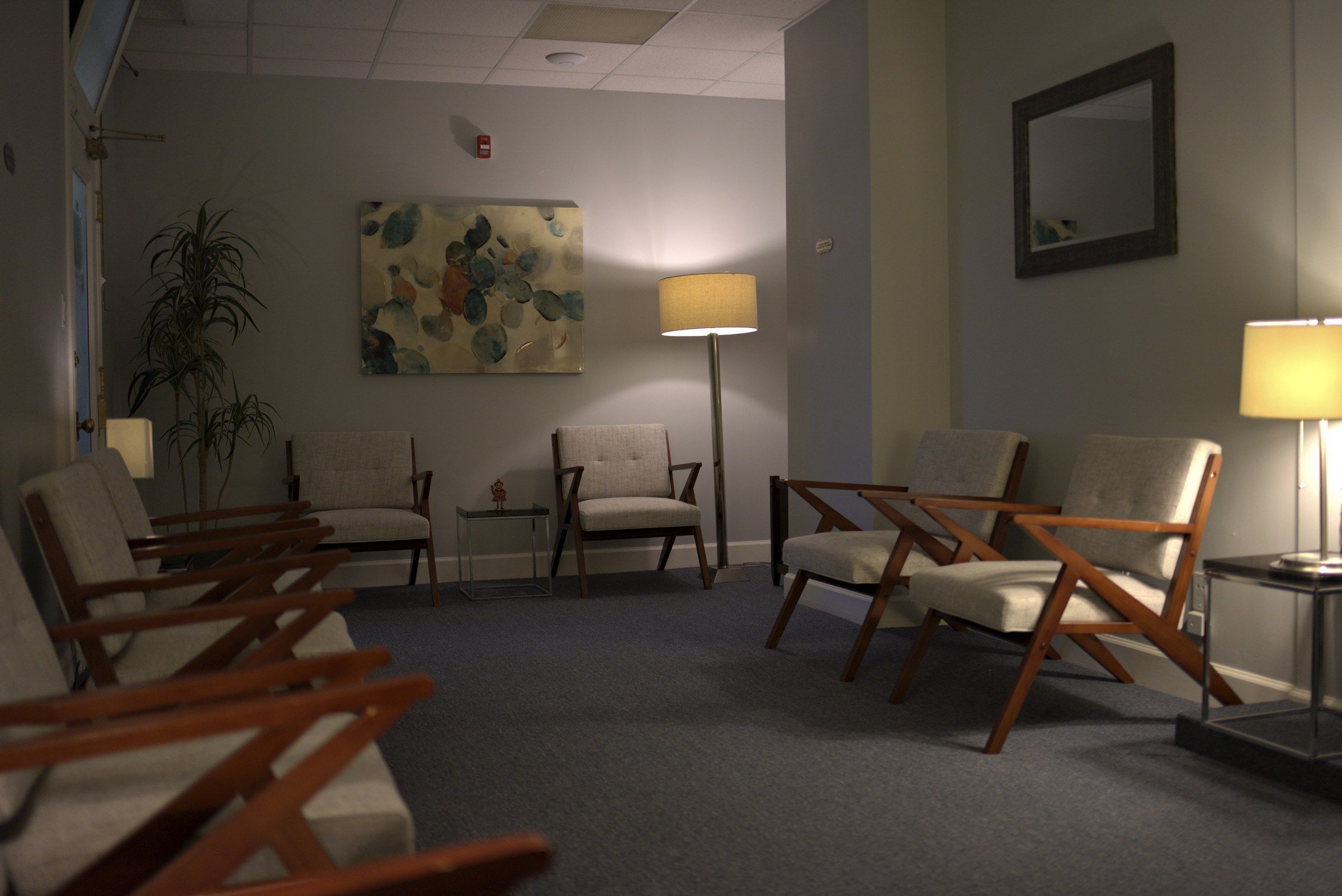 San Francisco waiting room with wooden armchairs, an abstract painting, floor lamps, and a tall plant.